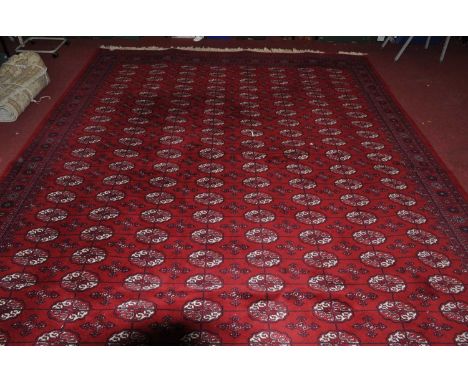 A large Persian style red ground machine made Bokhara rug (this item will be available for collection for either a short peri