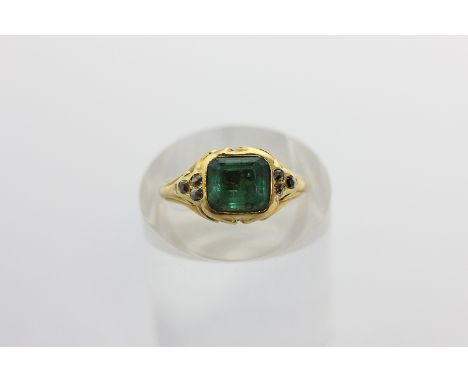 An emerald and diamond ring, the step cut stone rubover set with three old cut diamonds to each shoulder