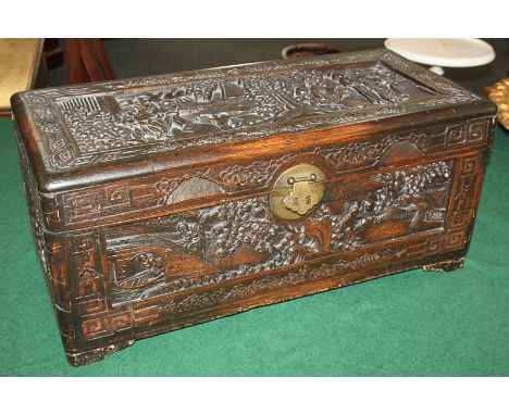 A Chinese camphor wood trunk, heavily carved with figure groups amidst trees, buildings and water, the interior with removabl