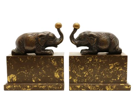 A pair of Art Deco style elephant bookends, modern, each balancing a ball on its trunk, raised on a gold-flecked resin plinth