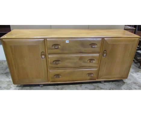 An Ercol light elm low sideboard enclosed by two doors flanking three drawers with oval dished handles and set on castors 155