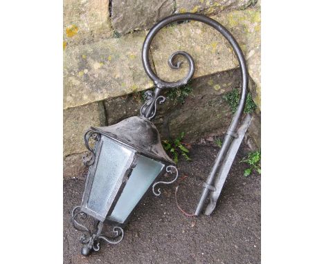 An ironwork wall mounted exterior lantern of hexagonal with frosted glass panels and scrolled combined bracket 
