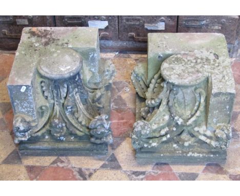 A pair of weathered carved natural stone architectural corner capitals with scrolling foliate detail, approximately 35 cm squ