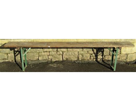 A stained trestle  bench with plank seat raised on folding painted iron supports, approx 220 cm long x 27cm wide 