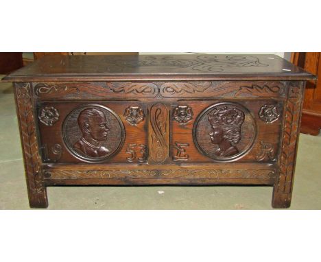 A reproduction old English style oak coffer with hinged lid and carved detail, front elevation with portrait panels and dated