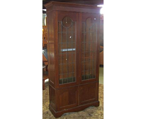 An Edwardian Arts &amp; Crafts oak bookcase, freestanding and enclosed by two pairs of panelled doors, the upper with leaded 