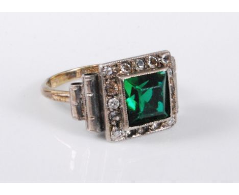 A 9ct gold and silver Art Deco style ring, the central green paste surrounded by a border of small white paste stones, 13mm w