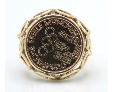 A yellow metal ring set with a 1972 Munich Olympics coin, coin & ring both electronically test as 14ct gold, 4.4g, size K