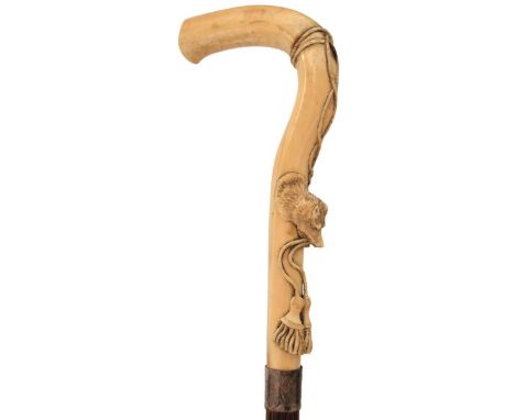 A 19TH CENTURY WALKING STICK, the ivory L shaped handle relief carved with a dog or wolf's head grasping tassels in its jaws,