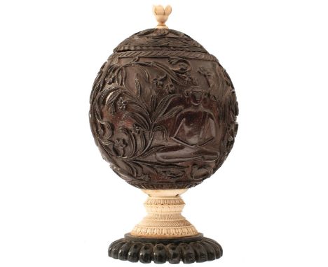 A 19TH CENTURY INDIAN COCONUT BOWL AND COVER, the body and lid carved with deities amidst scrolling foliage, the lid with car