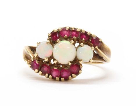 A gold opal and synthetic ruby ring, with a graduated row of round cabochon opals, claw set, to crossover shoulders grain set