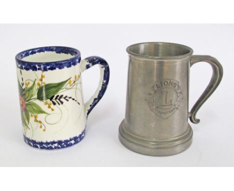 Two beer tankards, one Greek ceramic decorated with flowers and one pewter with glass bottom and the 'Lions' crest engraving.