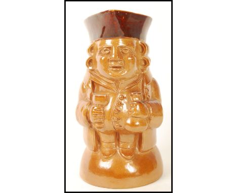 A large Doulton Lambeth seated Toby jug by Leslie Harradine raised on a domed base with flask and goblet. Impressed marks to 
