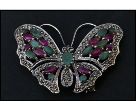 A sterling silver marcasite brooch in the form of a butterfly having ruby and emerald adorned wings. Weighs 13 grams.