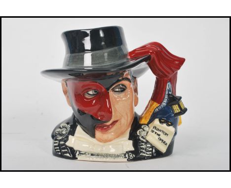 A Royal Doulton character jug depicting The Phantom of the Opera D7017 , handle modelled after a theatre curtain and coach li