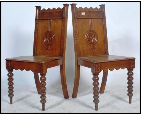 A pair of 19th century Victorian oak hall chairs being raised on carved tapering legs with panel seats and arched fielded pan