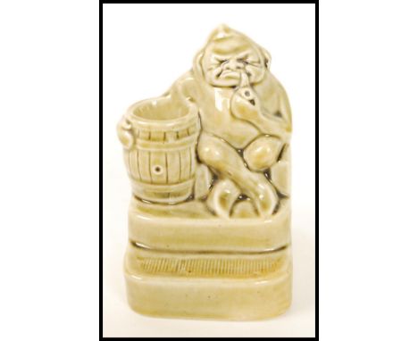 A Royal Doulton stoneware vesta matchstriker modelled as a pipe smoking gnome designed by Harry Simeon, modelled seated by a 
