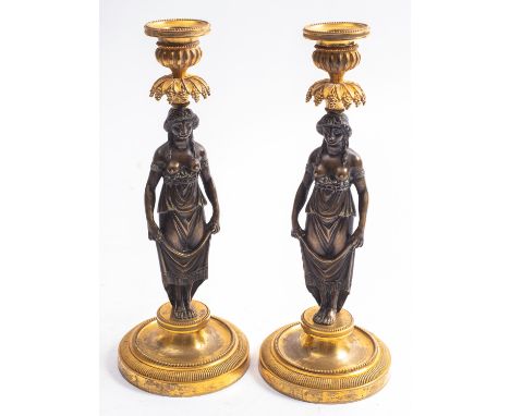 A pair of Empire patinated and gilt bronze figural candlesticks, early 19th century; with beaded and lobed urn sockets above 