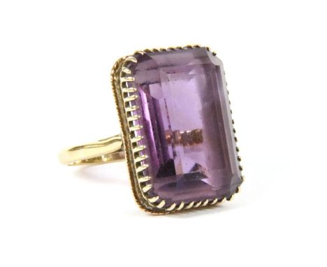 A gold single stone emerald cut amethyst ring, claw set to split shoulders and a plain polished shank, head tests as approxim