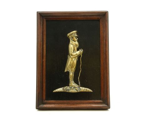 A cast brass relief of an East India Company man standing holding a stick, c.1820, applied to an ebony panel in a strut frame