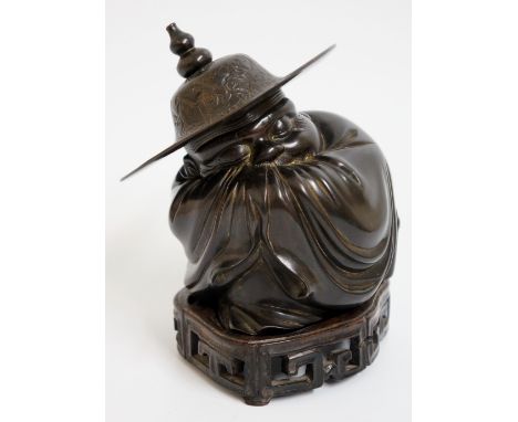 A 19th Century Chinese bronze figure of a sleeping immortal wrapped in his cloak, wearing a decorated wide brimmed hat with g