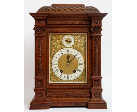 An oak cased mantel clock of inverted breakfront form the shallow domed top with rectangular tablet above a scale and leaf ca