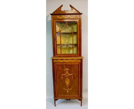 An Edwardian Sheraton revival standing corner cabinet with architectural pediment above a frieze inlaid with ribbon tied drap