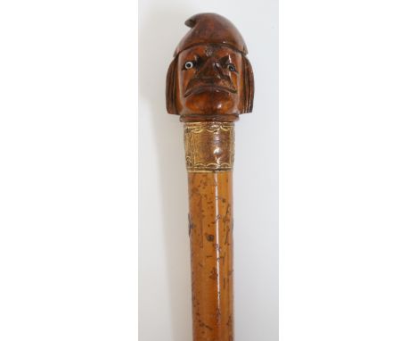 A Malacca walking stick, the terminal carved as a man with upturned nose and wearing a phrygian cap, inset glass eyes, white 