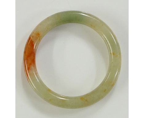 A plain circular jade bangle of celadon colour with brown inclusions, 8cm diameter