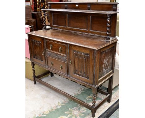 A 1930's oak sideboard, shelf and barley twist supports to galleried back, two short drawers flanked by linenfold doors to ba