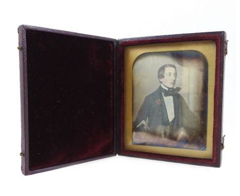 A Victorian daguerreotype portrait of a gentleman, in sitting pose holding a walking cane, contained in a burgundy leather an