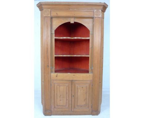 A Georgian pine corner cupboard, with outswept cornice and reeded decoration, shaped open shelves painted red, missing doors,