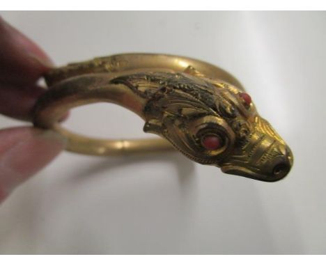 A late Victorian/Edwardian gilt metal snake bangle set with coral eyes and a coral pearl in its mouth 