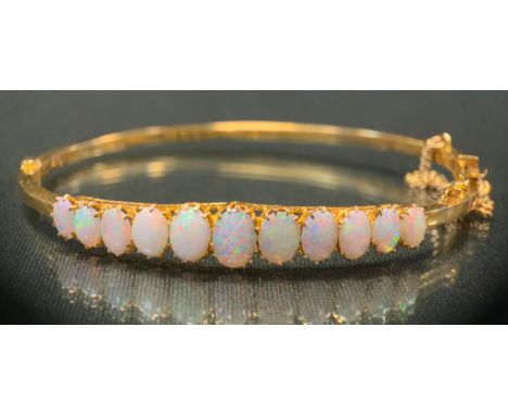An opal hinge bangle, set with eleven oval graduated opal cabochons, ranging from approx 7mm x 1.5mm to 5mm x 1.3mm, vibrant 