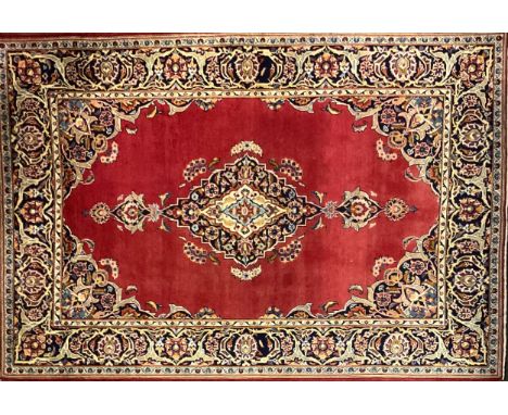 A Kashan rug / carpet, having a central diamond shaped medallion in a field of light red, within margins of deep indigo, pale