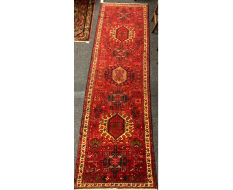 A Heriz runner carpet, hand knotted in red, black, cream, and green, with a row of three hexagonal medallions in a field of s