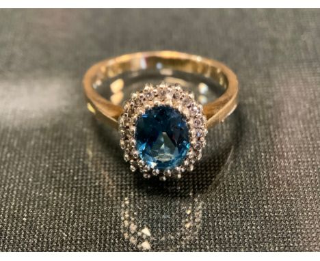 A diamond and blue topaz ring, central oval vibrant pale blue topaz approx 0.75ct surrounded by twenty diamond accents, total