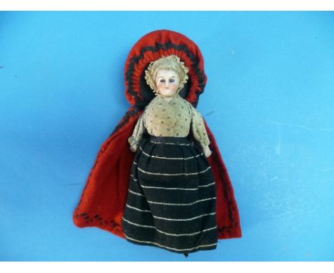 A late 19th century continental bisque head and shoulders Doll, dressed in skirts and red cloak, 7in (17.75cm) high.