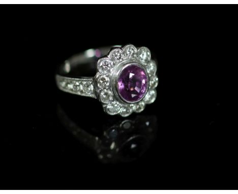 A modern 18ct white gold, pink sapphire and diamond cluster ring,with diamond set shoulders, the oval cut sapphire weighing a