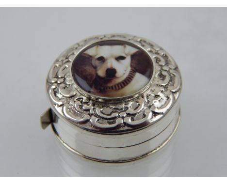 A novelty circular white metal tape measure, decorated with a small enamel plaque depicting a white dog. 
