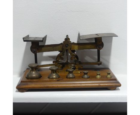 An antique set of brass Postal Scales, on wooden base, with complete set of six weights, the base 21cm long. 