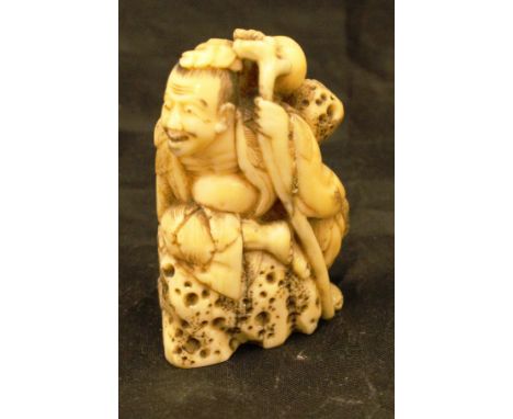 A 19th Century Japanese Meiji period carved ivory netsuke as Sennin seated on rocks, a staff at his side