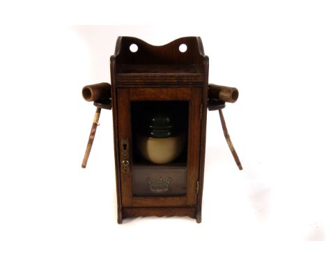 An oak smokers cabinet, the glazed front cabinet opens to reveal interior drawer and ceramic pot, with two hinged external pi