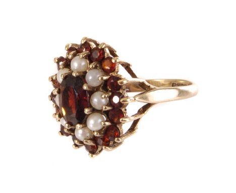 A 9ct gold, garnet and seed pearl cluster style ring, the oval cut central garnet surrounded by a single oval row of seed pea