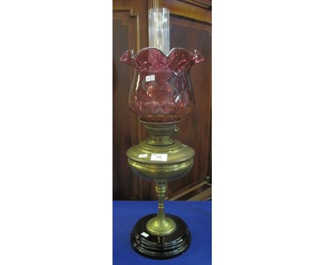 Brass oil lamp with pedestal support on ceramic base, cranberry coloured shade with clear chimney.(B.P. 24% incl. VAT)