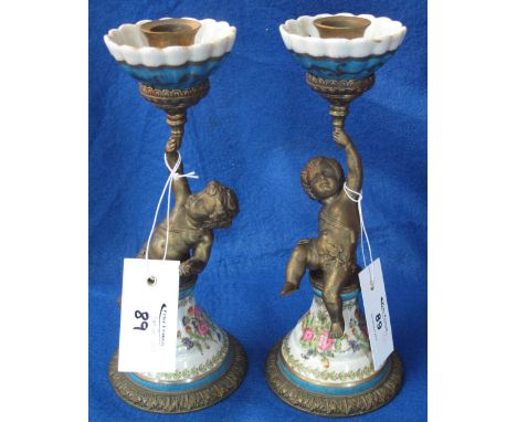 Pair of gilt metal and ceramic candlesticks in the form of putties supporting torches, printed mark to base. 23cm. (2)(B.P. 2