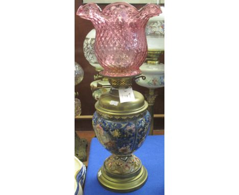 Brass double burner oil lamp, having glazed foliate design ceramic baluster shaped body on a brass foot with cranberry glass 