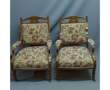 A pair of Edwardian mahogany armchairs with marquetry inlay having floral tapestry upholstery raised on turned legs and casto