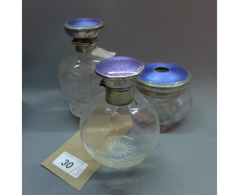 An early 20th century glass cosmetic jar, with silver and guilloche enamel top, together with a matching cosmetic jar (a/f), 