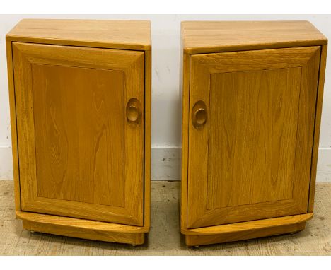 A pair of Ercol elm side cabinets, of trapeze shape, with a cupboard door enclosing a shelf, standing on a plinth base, 68.5c